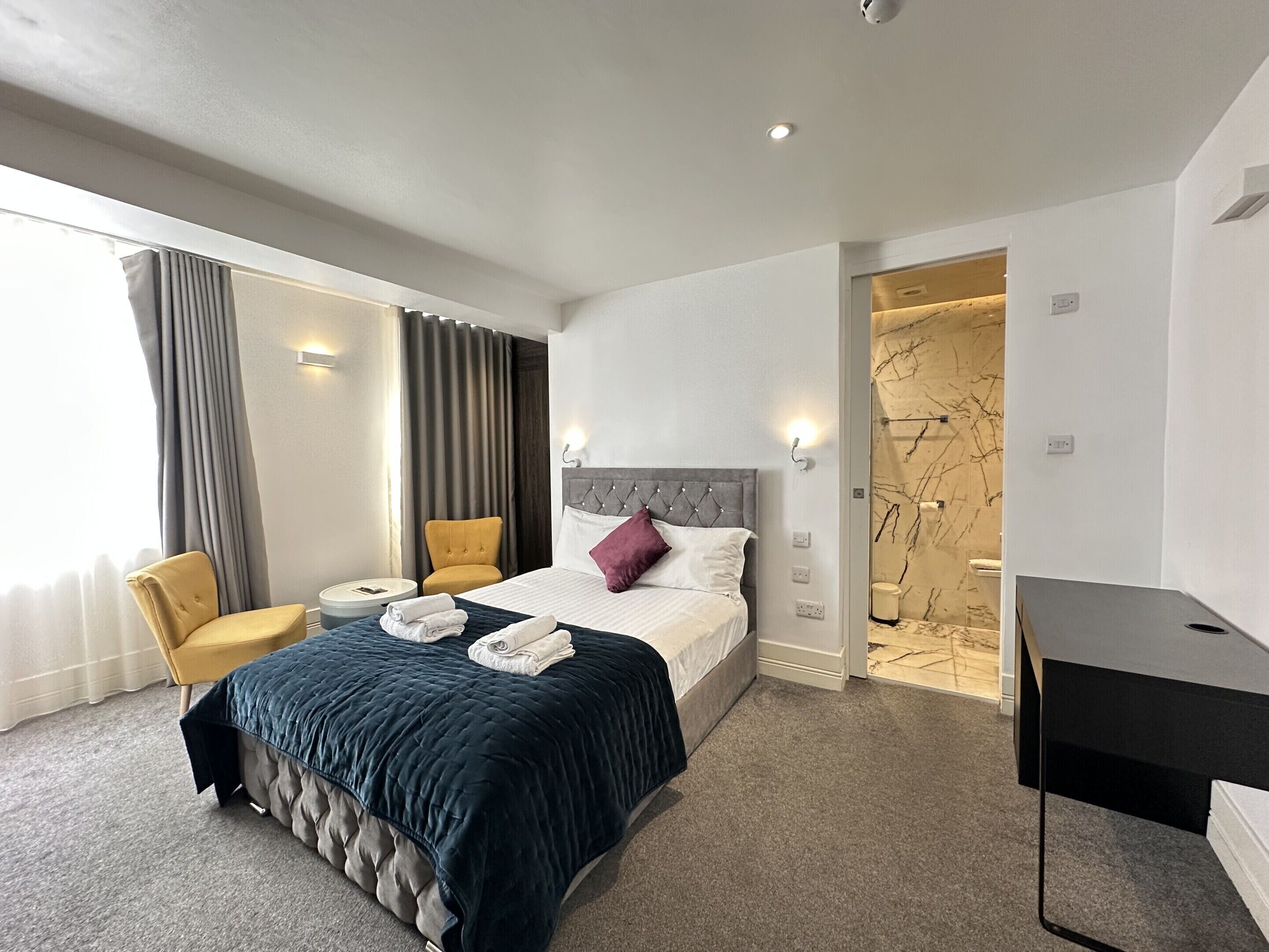 A hotel room with a bed, a chair, a desk, and a bathroom visible through an open door.