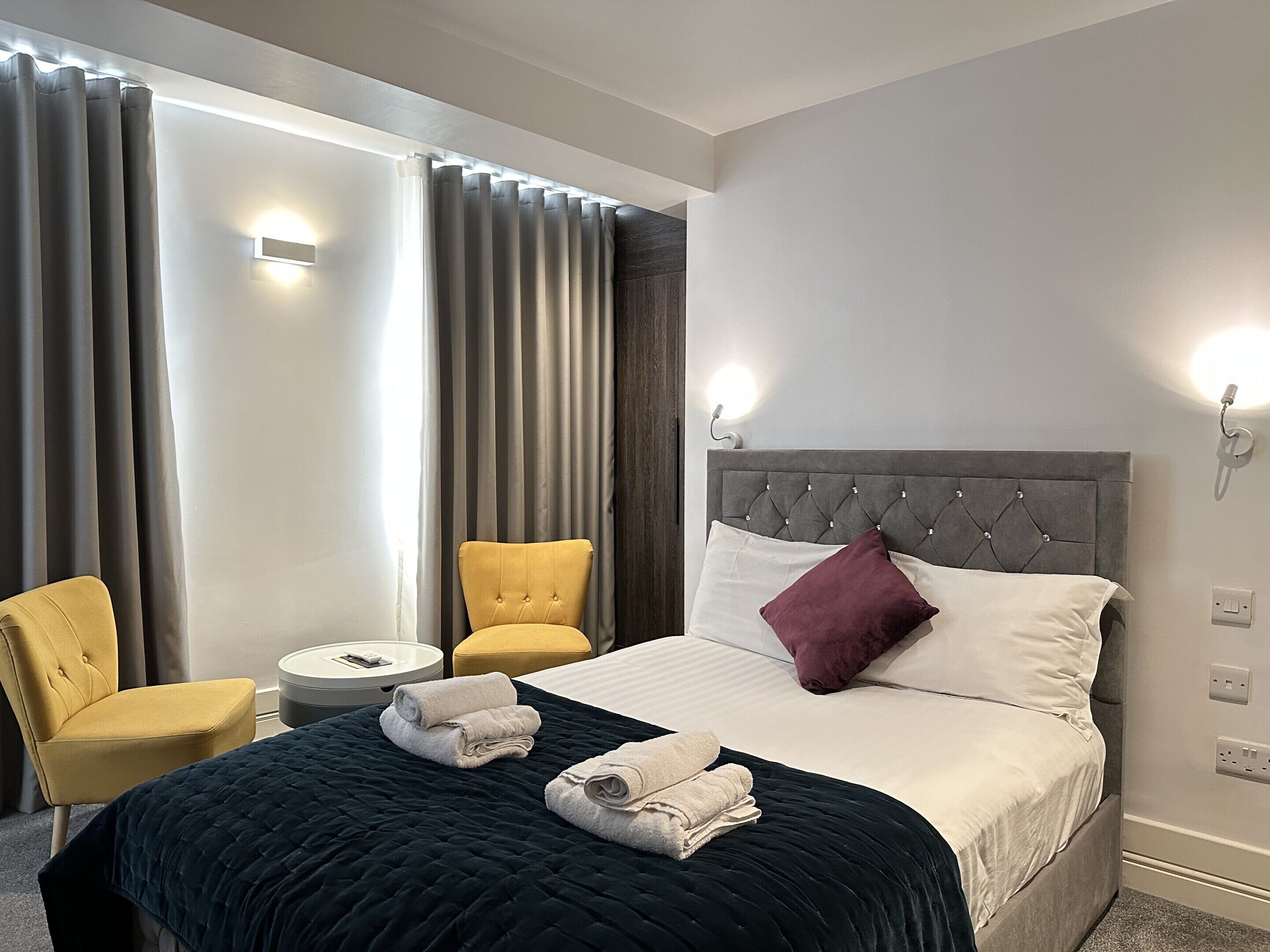 Ein Hotelzimmer mit einem Bett, zwei Stühlen, einem kleinen Tisch und einem Fenster mit Vorhängen.