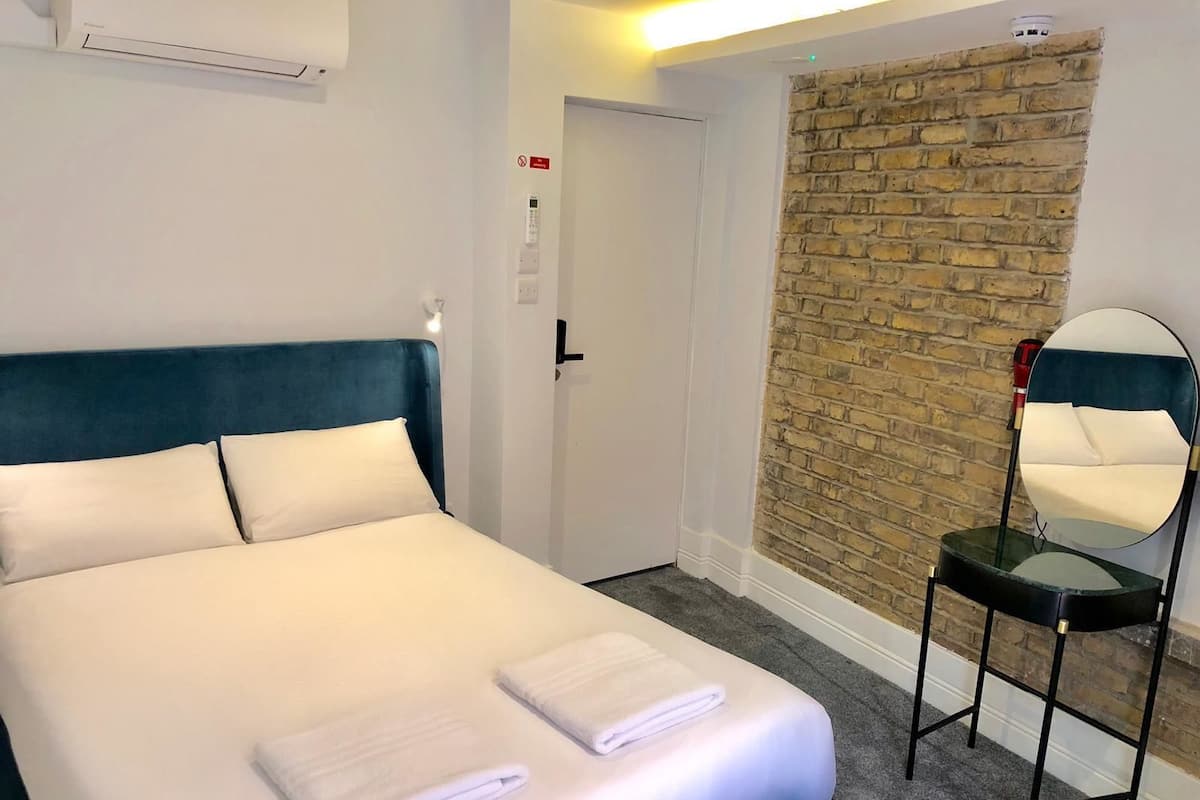 A hotel room with a bed, a mirror, and a brick wall.