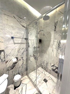 A modern bathroom with a glass-enclosed shower, marble walls, and a toilet. - Widegate Residential (London)