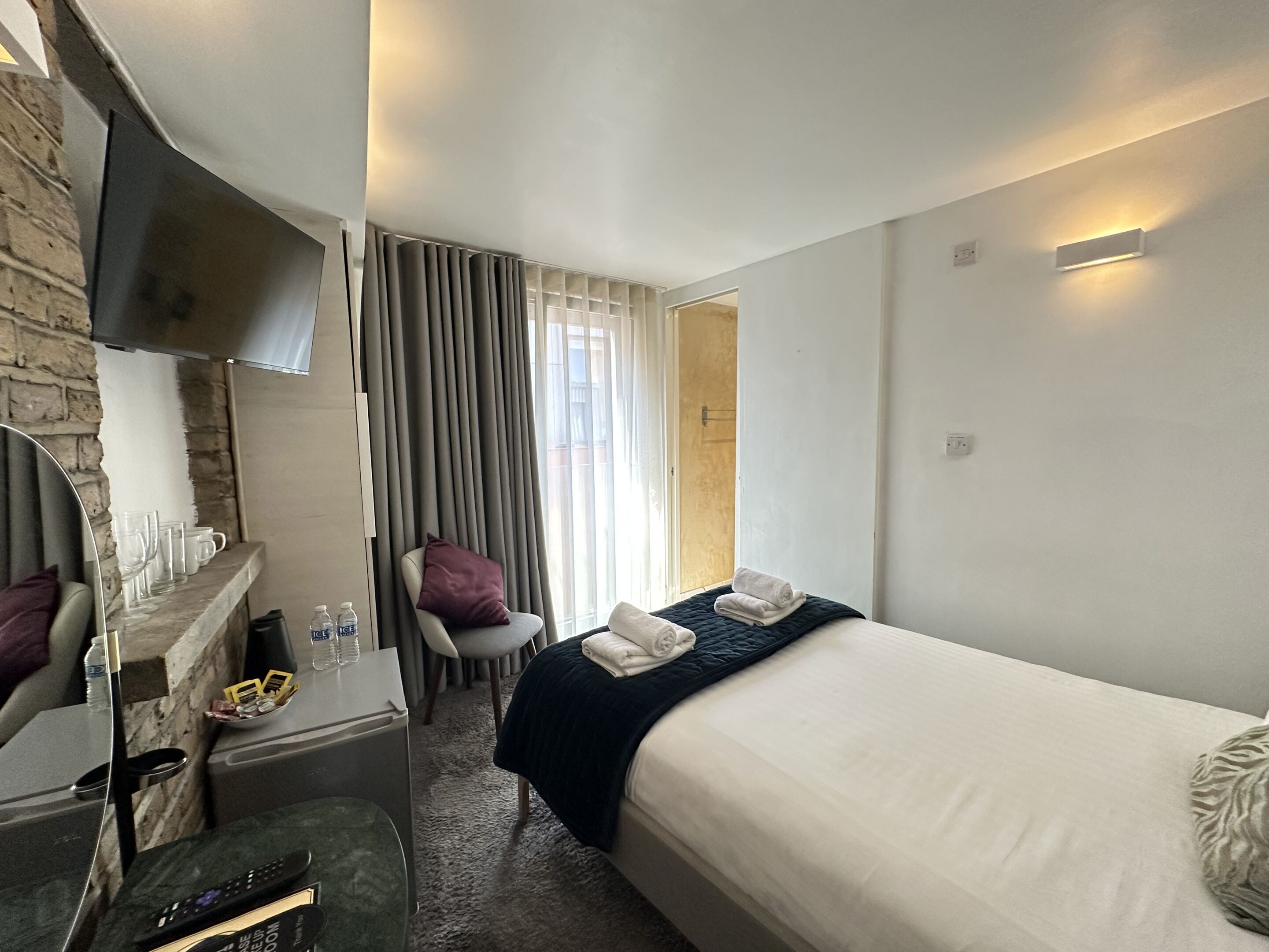 Hotelkamer met een bed, bureau, stoel, televisie en een raam met gordijnen.