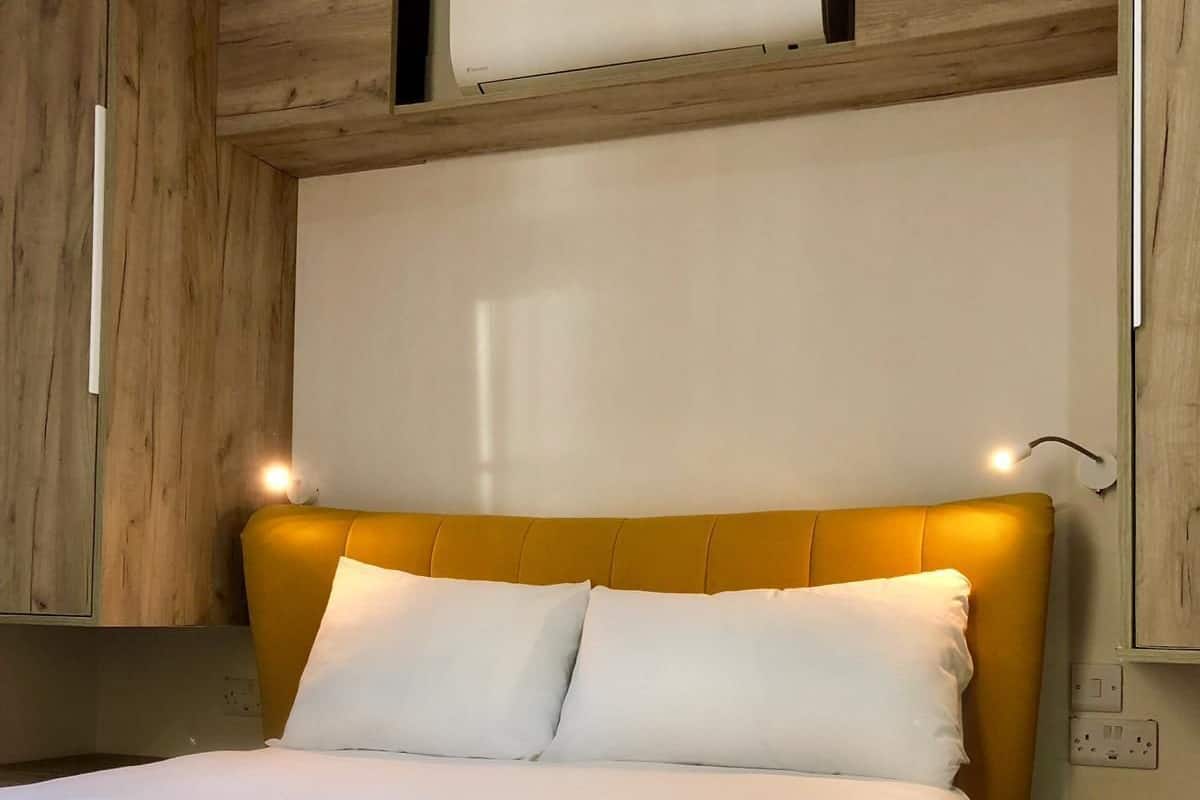 A bed with a yellow headboard, white bedding, and a bedside table with a lamp.