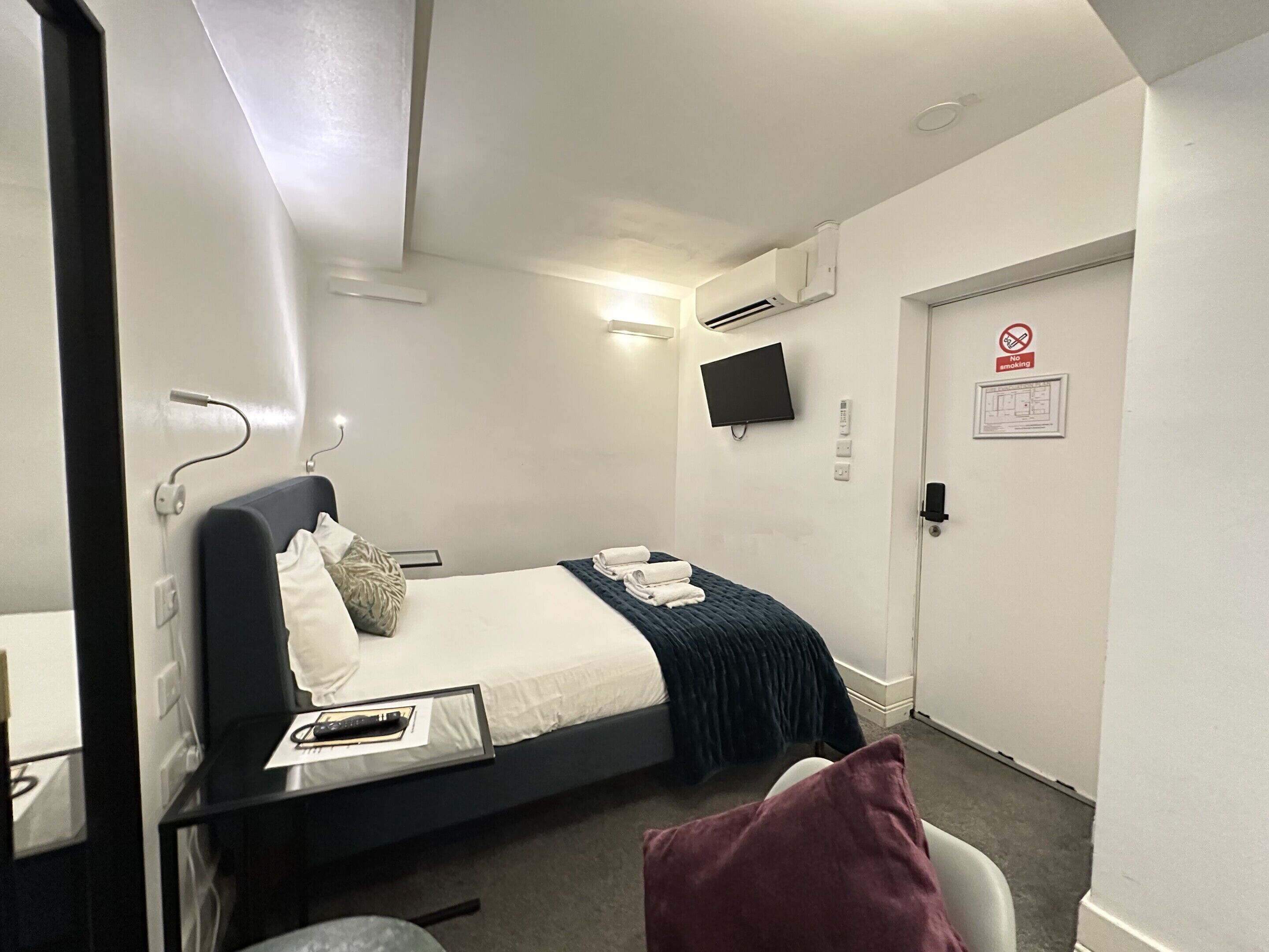 Ein Hotelzimmer mit Bett, Fernseher, einer Tür mit Rauchverbot-Schild und einem kleinen Tisch mit Fernbedienung.