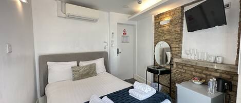 A hotel room with a bed, a bedside table, a mirror, a TV, and a wall-mounted shelf with glasses.