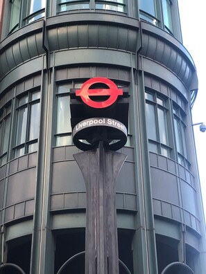 Un bâtiment sur lequel on peut voir une grande enseigne circulaire rouge, avec un « e » blanc au centre et le texte « Liverpool Street » en dessous.