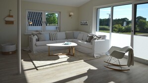 Un salon moderne avec un canapé d’angle, une table basse ronde et un fauteuil à bascule.