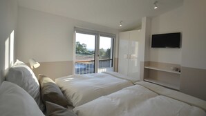 Une chambre d’hôtel moderne dotée d’un grand lit, d’un téléviseur fixé au mur et d’un balcon offrant une vue sur le paysage.