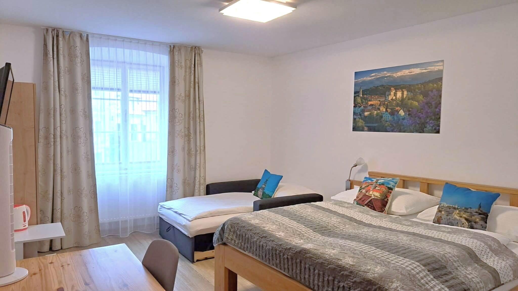A hotel room with a bed, a desk, a chair, a TV, and a painting on the wall.