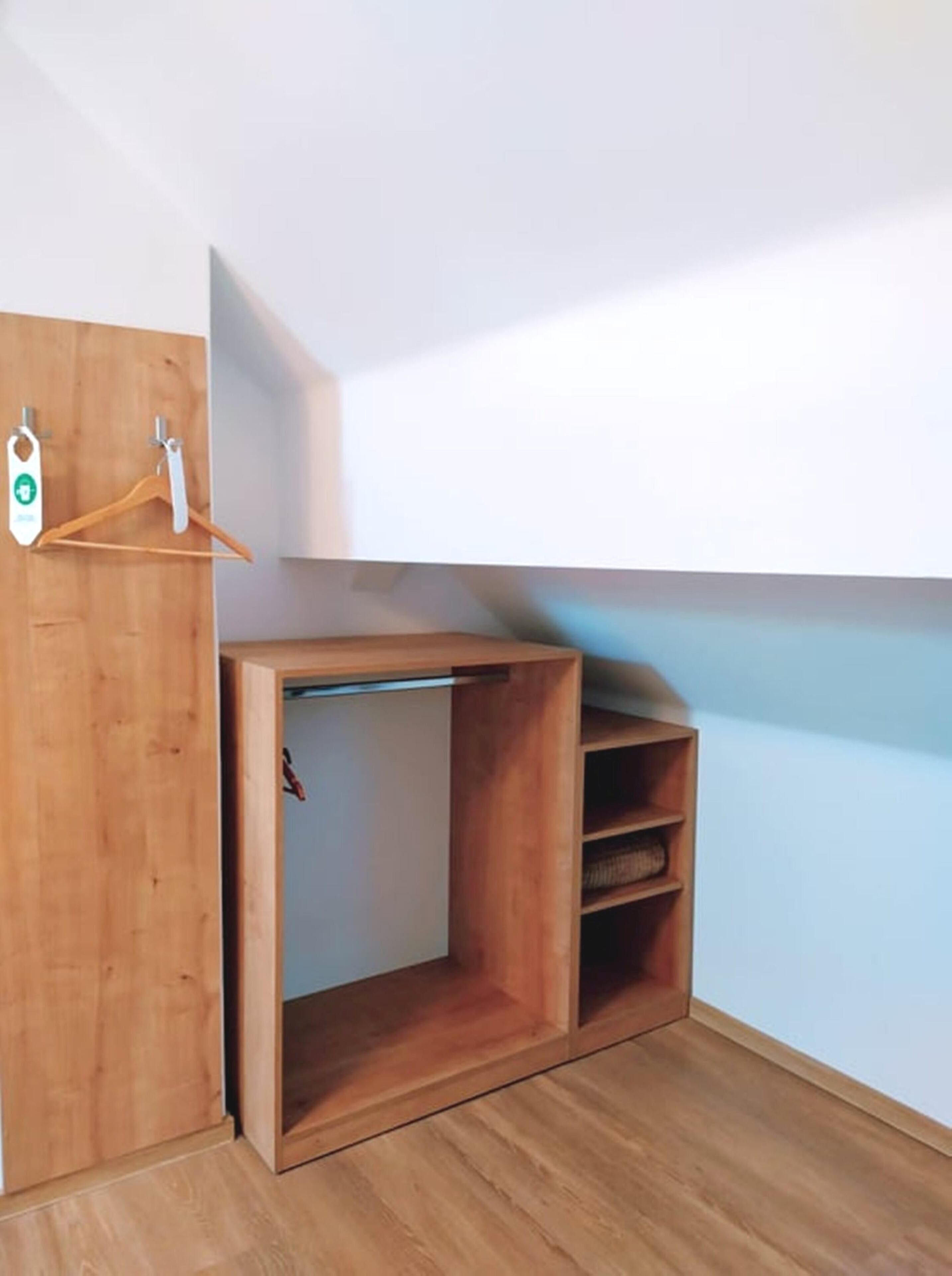 A corner of a room with a wooden wardrobe, a hanging rack, and a shelf unit.