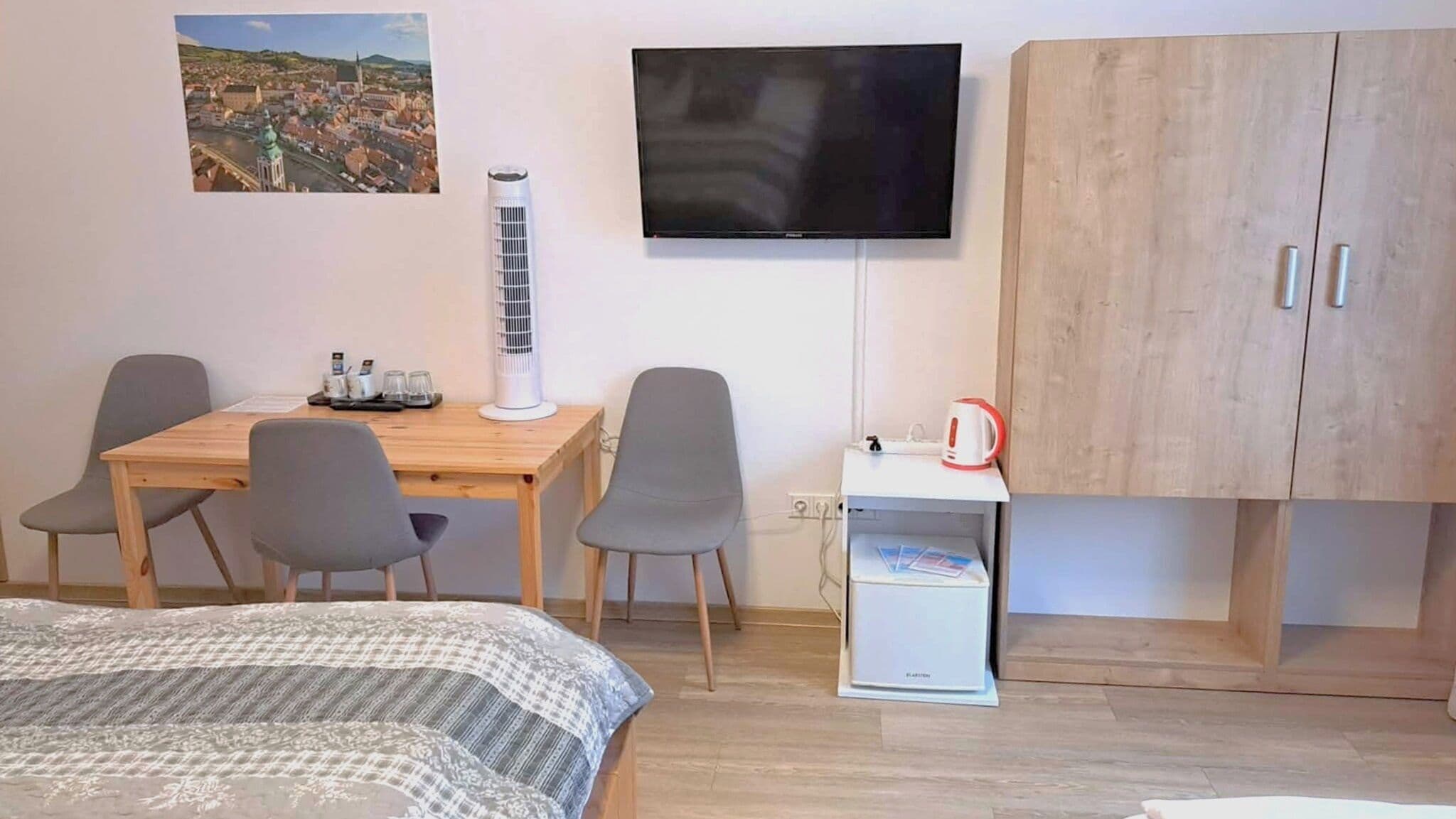Ein Hotelzimmer mit Bett, Schreibtisch mit Stühlen, Fernseher, Schrank und kleinem Tisch mit Wasserkocher.