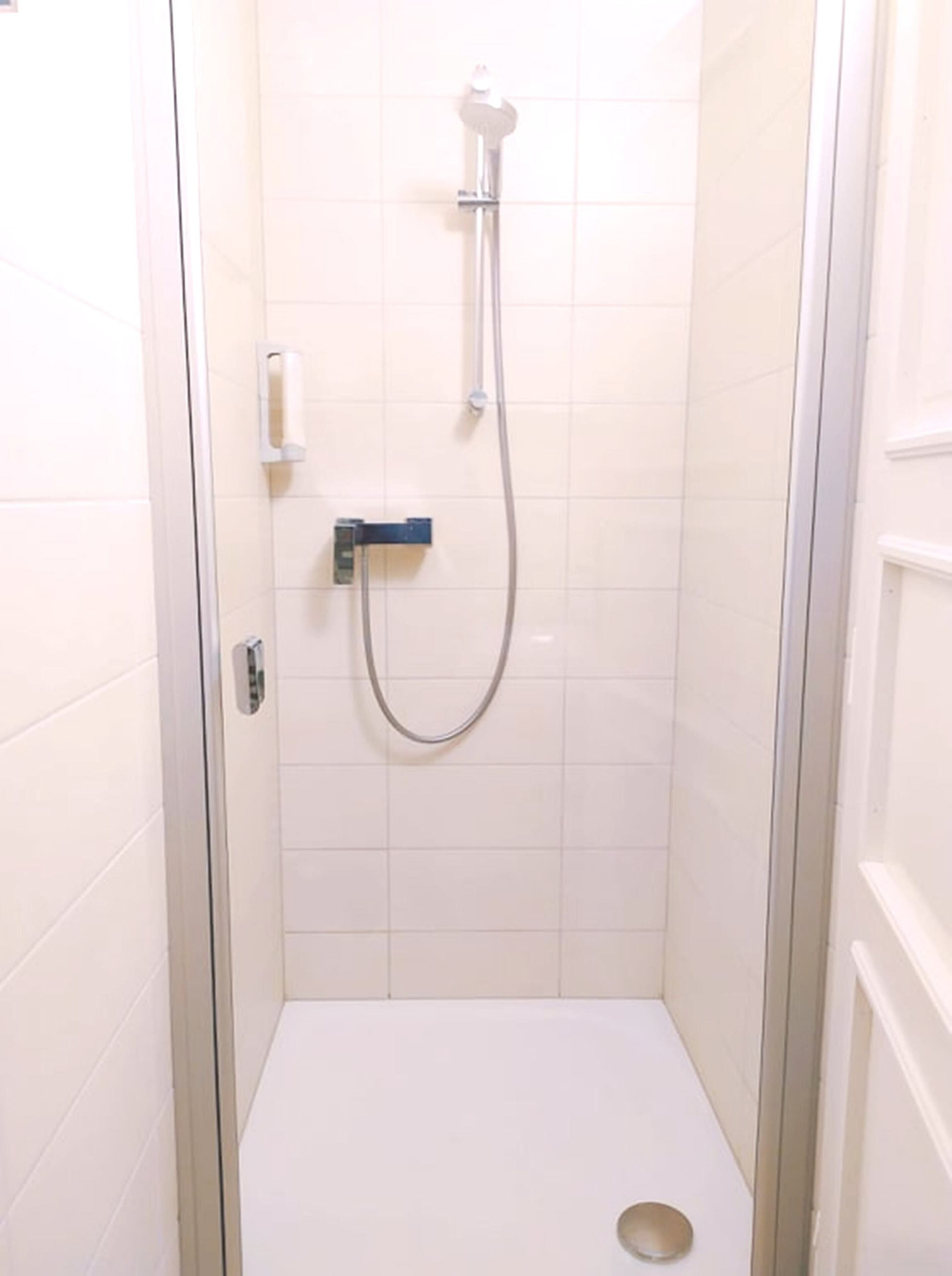 A small, enclosed shower stall with a handheld showerhead and a control panel.