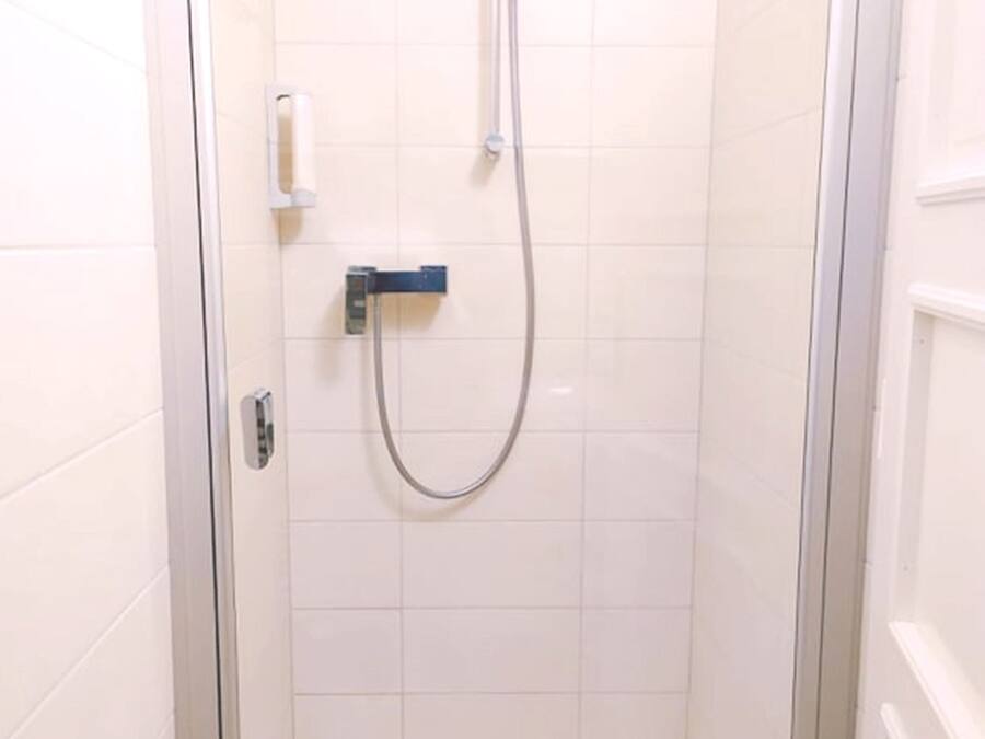 A small, enclosed shower stall with a handheld showerhead and a control panel.