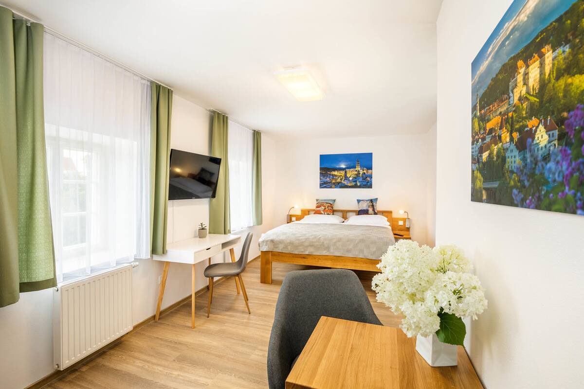 A hotel room with a bed, a desk, a chair, a TV, and a painting on the wall.