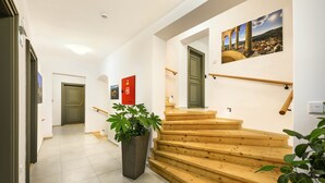 A staircase with wooden steps and a handrail, leading to a landing with a red door and a wall-mounted picture. - Hotel Garni Villa Areka (Cesky Krumlov)