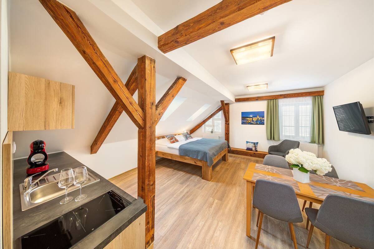 A compact, modern room with a loft bed, a dining area, and a kitchenette.