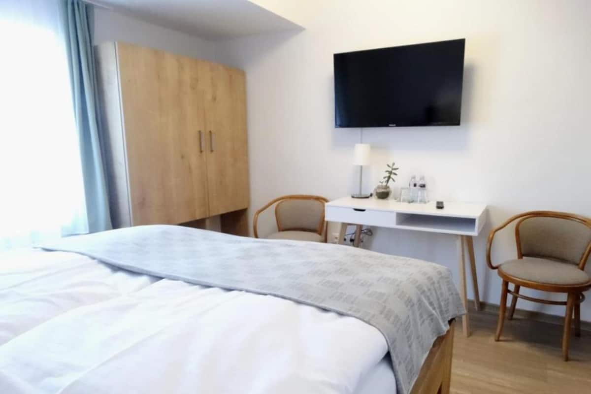 A hotel room with a bed, a desk, two chairs, a television, and a wardrobe.