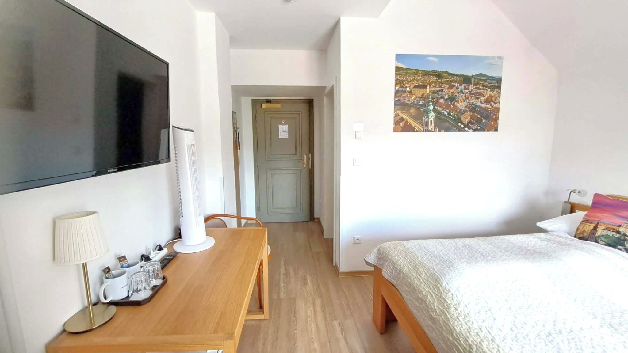 Une chambre d’hôtel avec un lit, un bureau doté d’une lampe, une télévision et un tableau représentant un paysage urbain.