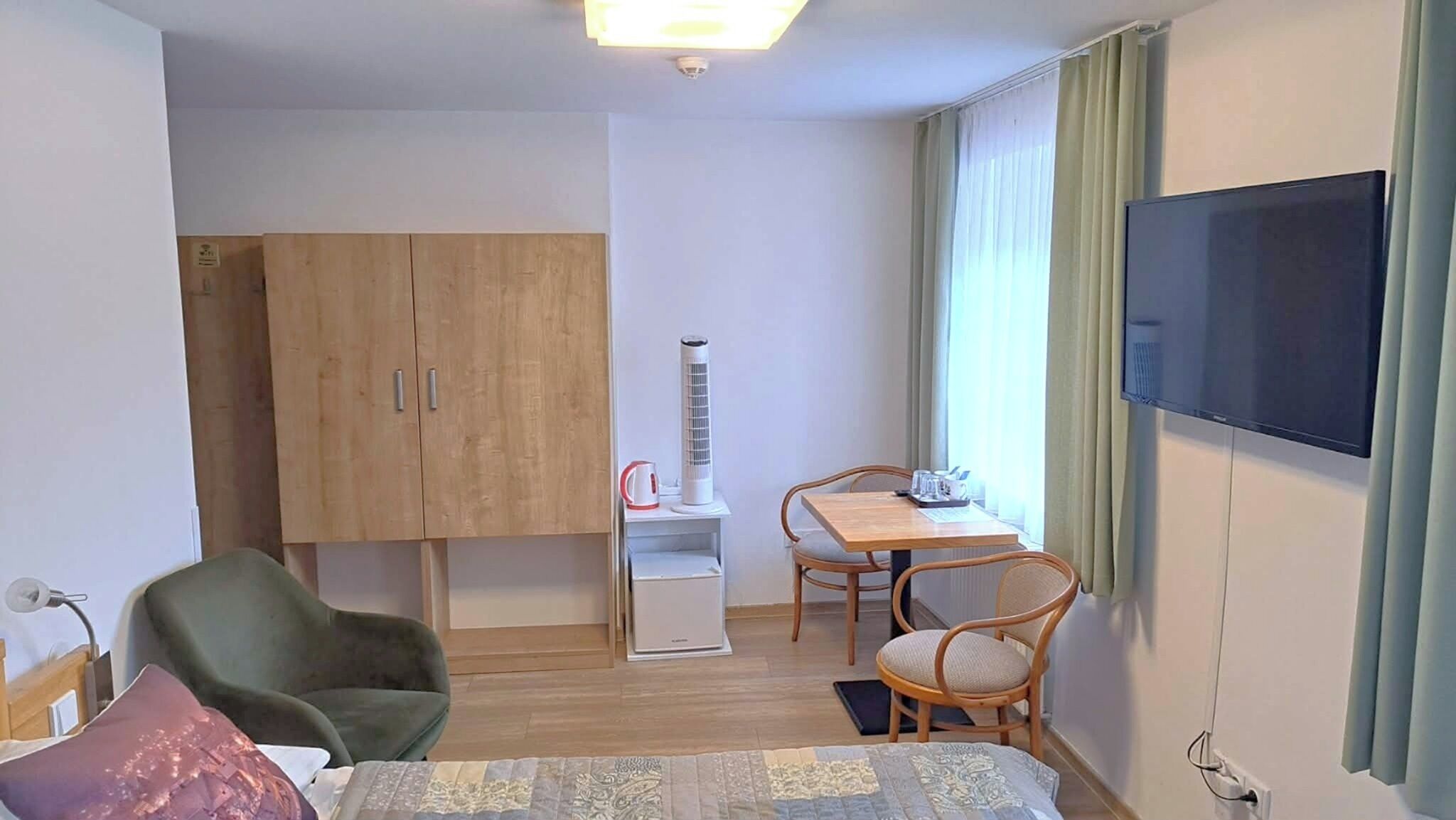 Ein Hotelzimmer mit einem Bett, einem Schreibtisch mit Stuhl, einem Fernseher und einem Kleiderschrank.