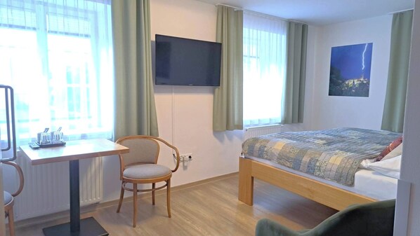 A hotel room with a bed, a desk, a chair, a television, and a window with curtains.