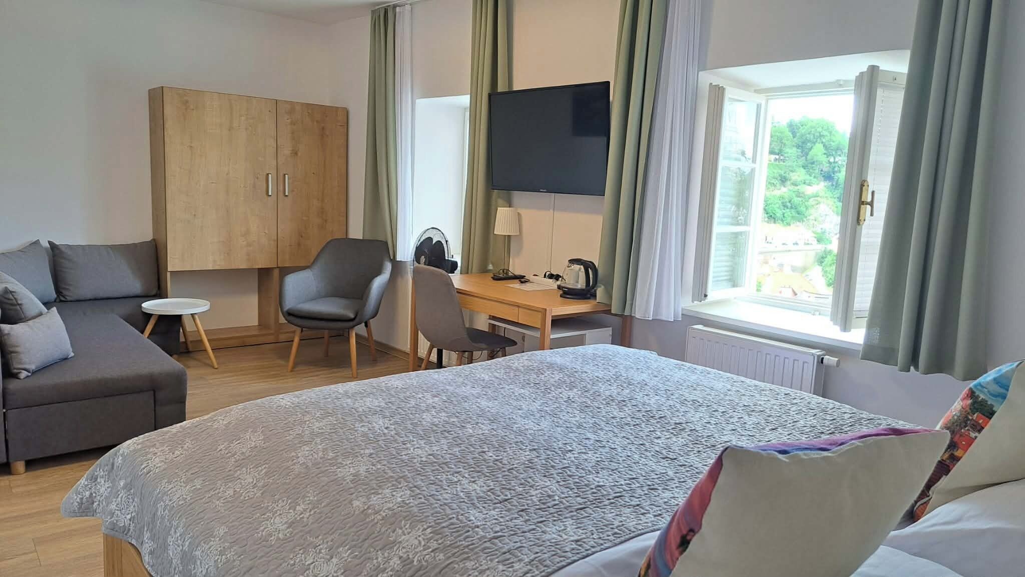 Een hotelkamer met een bed, bureau, stoel, bank, televisie en garderobe.
