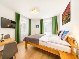 Una habitación de hotel moderna con una cama de madera, un escritorio, una silla, un televisor de pantalla plana y cortinas verdes.