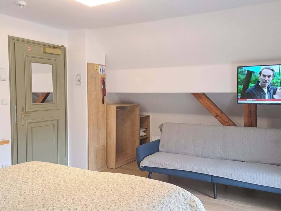 Una habitación con una cama, un televisor fijado a la pared, un armario de madera y una mesita con una tetera.