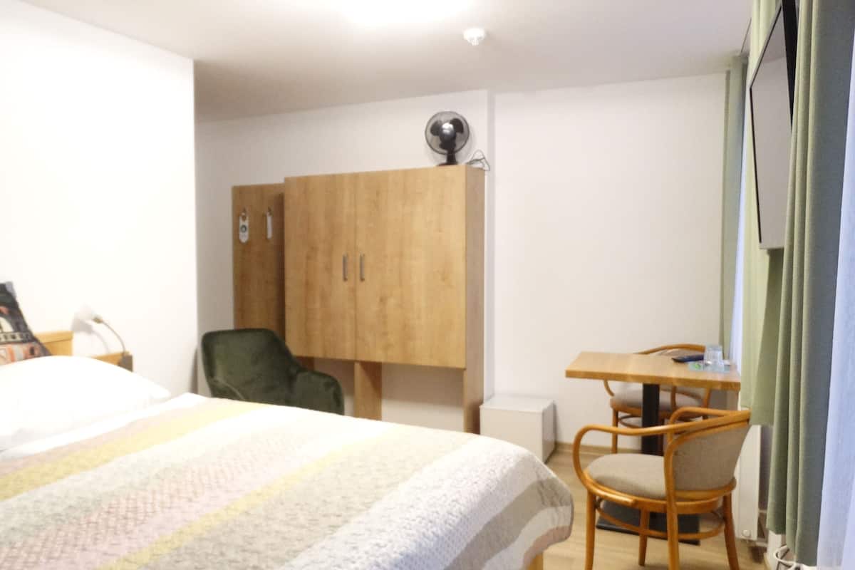 A bedroom with a bed, a desk, a chair, a wardrobe, and a painting on the wall.