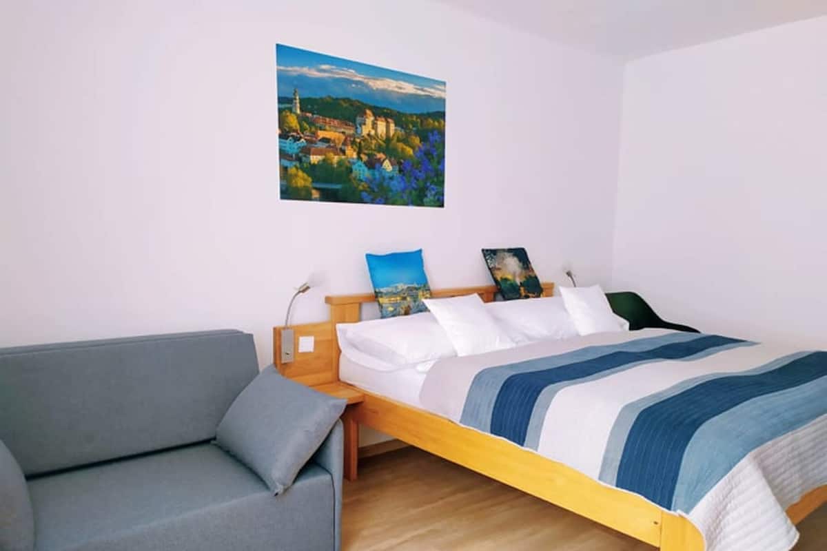 A bedroom with a bed, a grey sofa, and a painting on the wall.