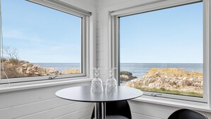 Una stanza con un tavolo rotondo e due sedie, vista sul mare e costa rocciosa.