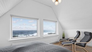 Una camera da letto con un letto grande, due finestre vista oceano, un tavolino con sedie e una pianta in vaso.