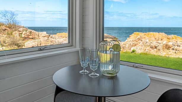 Un tavolo con tre bicchieri e una caraffa d'acqua, con vista su una costa rocciosa.