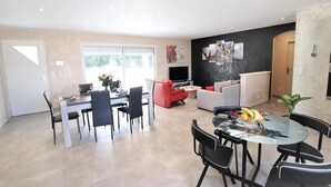 Een moderne woonruimte met een eethoek, een bank, een televisie en kunstwerken aan de muur.