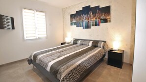 Een slaapkamer met een bed, twee nachtkastjes, een televisie en een raam met jaloezieën.