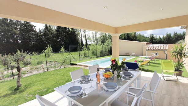 Een terras met een tafel voor vier personen, met uitzicht op een zwembad en een tuin.
