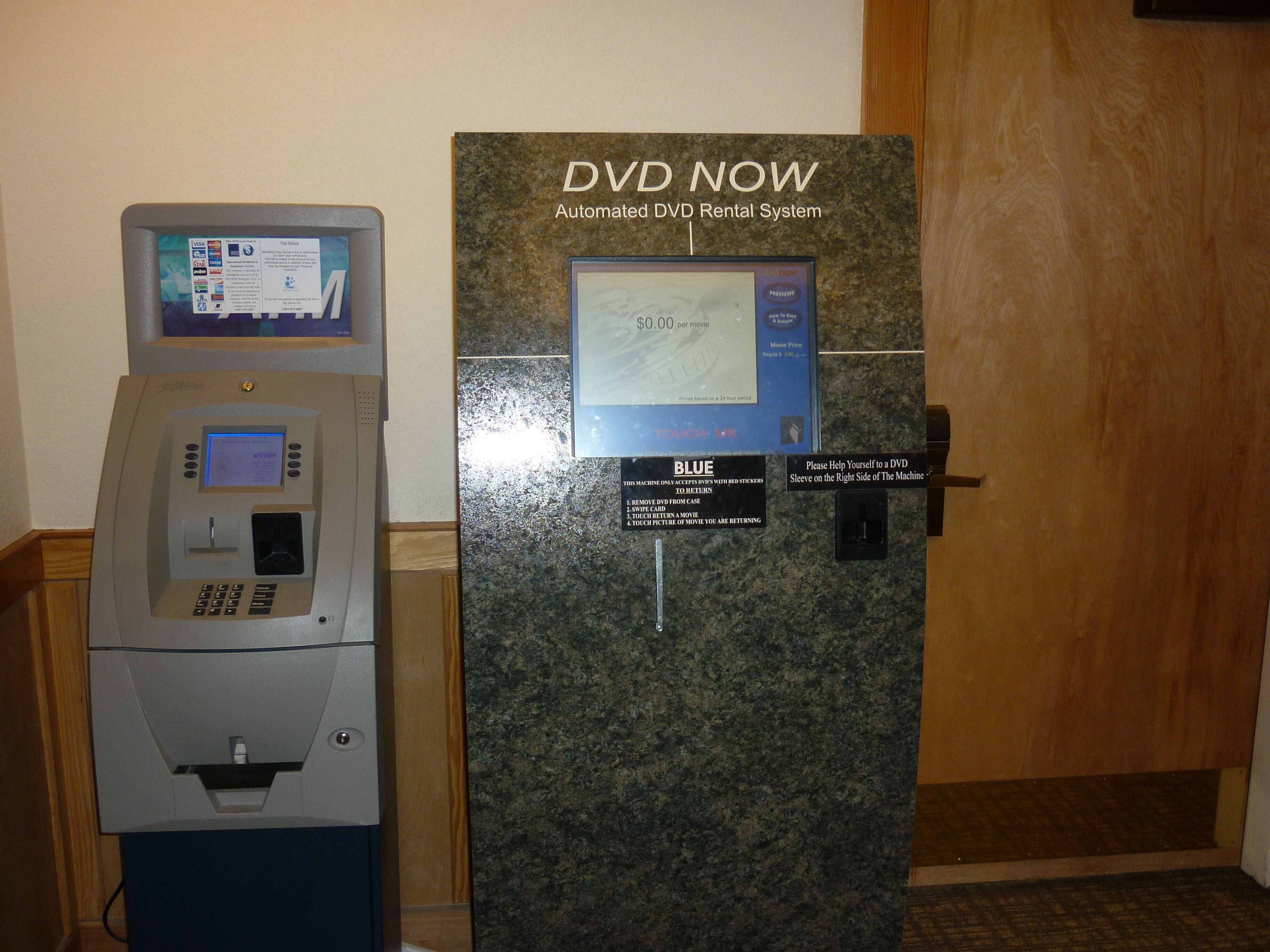A DVD rental kiosk with a screen and card reader, labeled 'DVD NOW' for automated rentals.