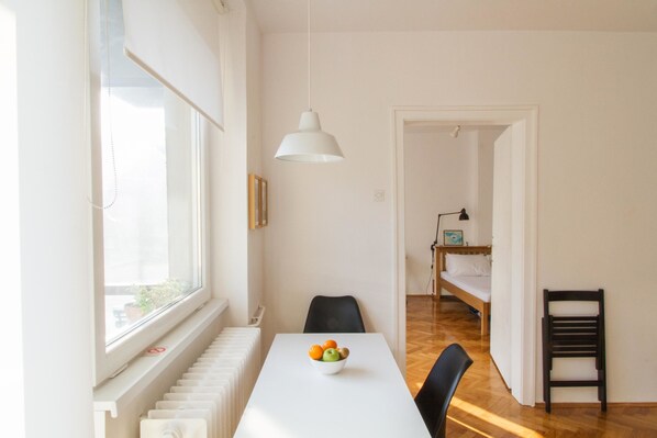 A bright, well-lit room with a white table, a bowl of fruit, a black chair, and a white pendant light.