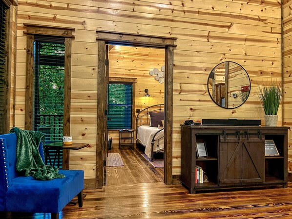 Interior de una cabaña de madera con un sofá azul, una cama, un espejo y una estantería.