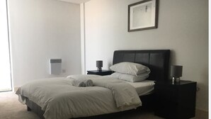 Quarto com cama, duas mesas de cabeceira, um criado-mudo, um quadro na parede e um radiador.