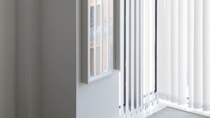 Quarto com uma janela grande, paredes brancas e vista para edifícios.