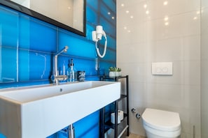 A bathroom with a white sink, blue-tiled wall, a white toilet, and a shelf with toiletries. - 4 Elements Old Town Views Rooms (Trogir)