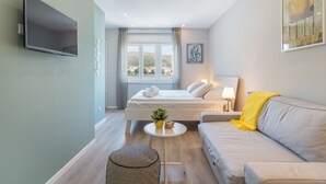A modern hotel room with a bed, a sofa, a TV, and a window with a view of the city. - 4 Elements Old Town Views Rooms (Trogir)