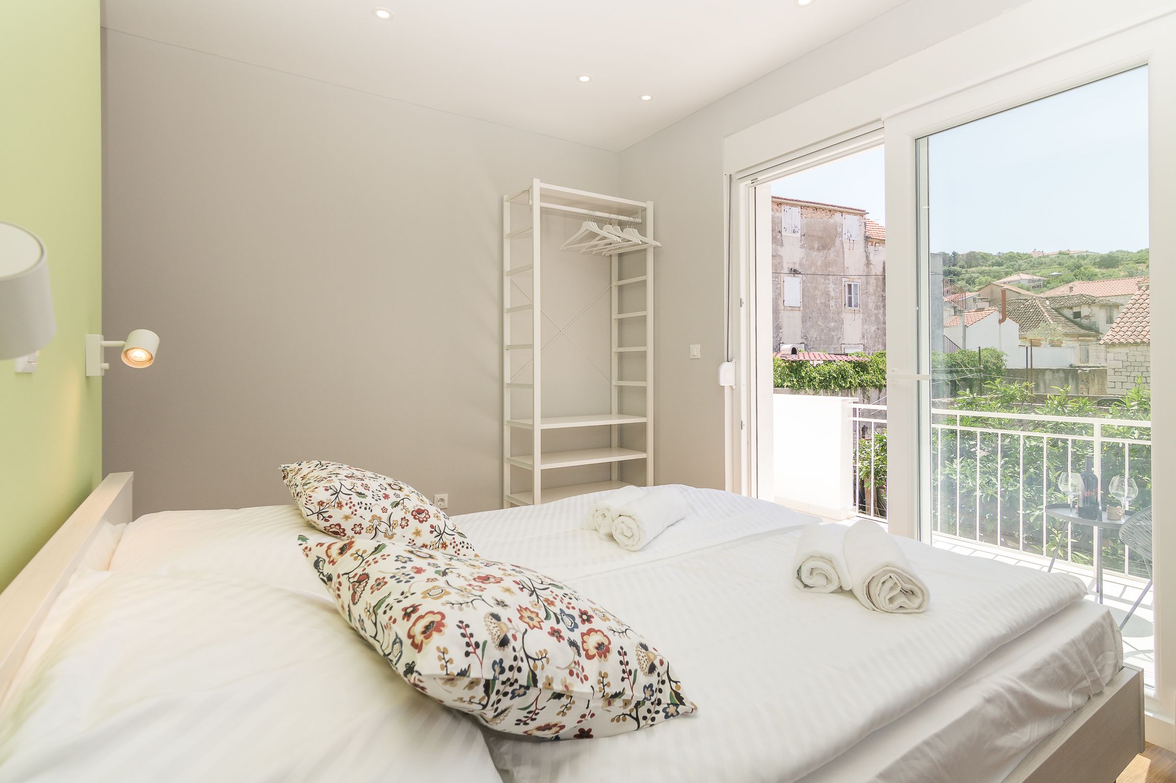 Un dormitorio con cama, un armario blanco y un balcón con vistas a edificios.