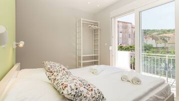 Un dormitorio con cama, un armario blanco y un balcón con vistas a edificios.
