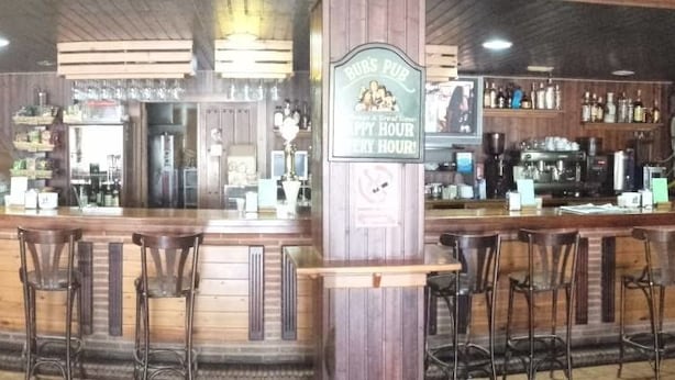 A bar area with wooden bar counters, stools, and a sign indicating a happy hour. - Hostel Restaurant Leyvamar (Guadahortuna)