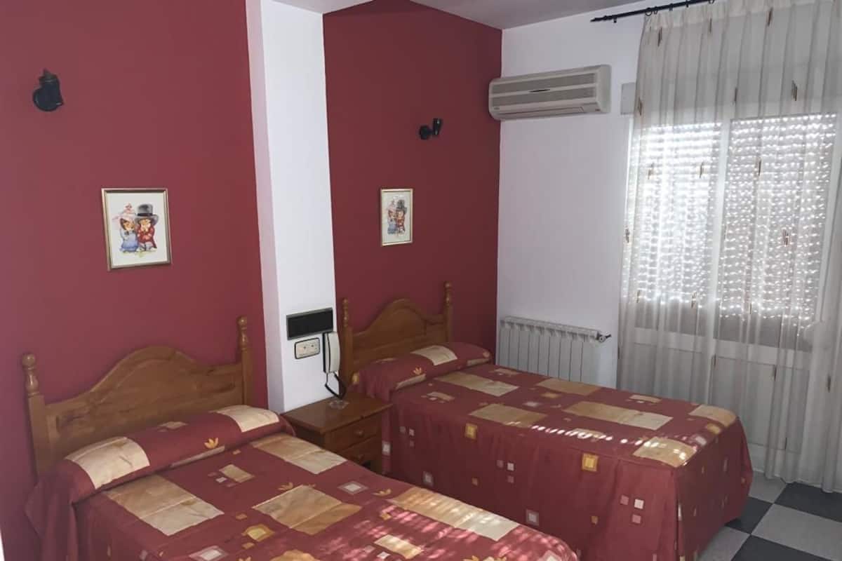 Ein Zimmer mit zwei Betten, einem Heizkörper, einer Klimaanlage und einem Fenster mit Vorhängen.