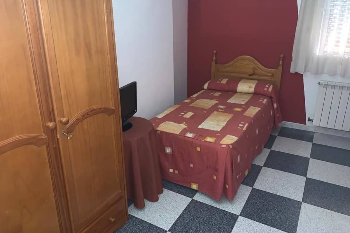 Ein Schlafzimmer mit Schachbrettmuster-Boden, einem hölzernen Bett, einer roten Wand und einem Holzschrank.