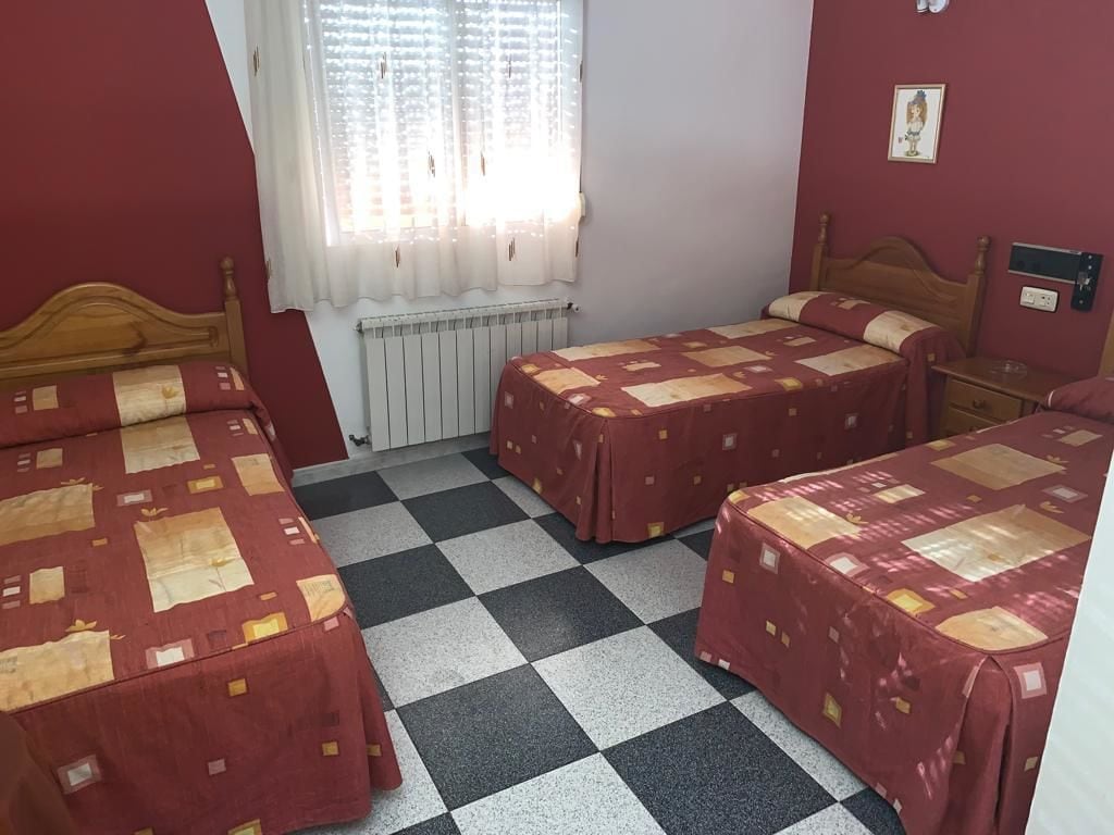 Una habitación con dos camas, un radiador, una ventana con cortinas y un interruptor de luz en la pared.