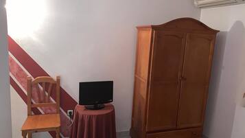 A room with a wooden chair, a small round table with a television, and a large wooden wardrobe.