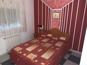 A room with a checkered floor, a bed with a patterned bedspread, a radiator, and a wall with vertical stripes and a framed picture. - Hostel Restaurant Leyvamar (Guadahortuna)