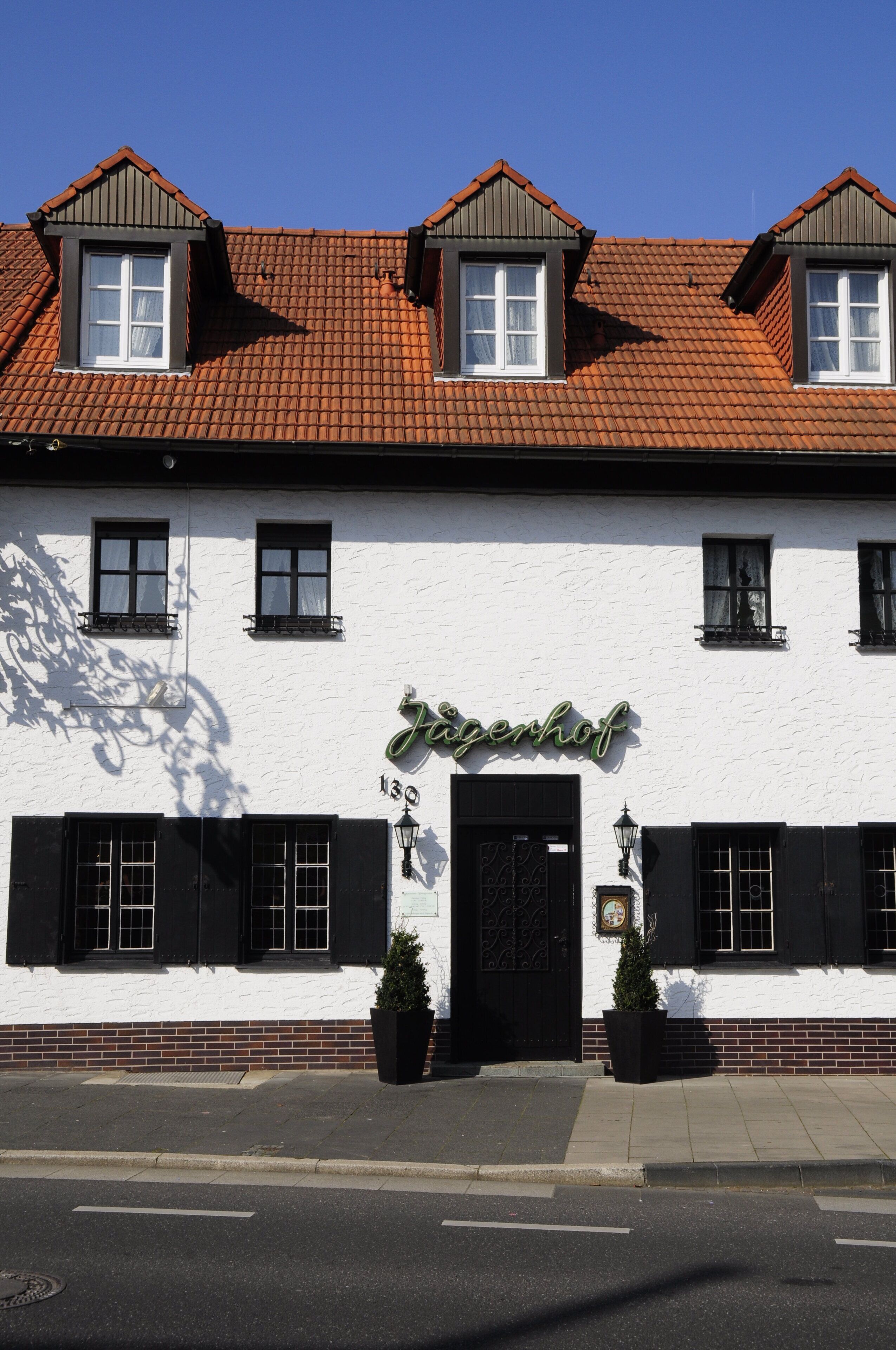 A white building with a black roof and black shutters, labeled "Jagenhof" with a number "130" above the door.